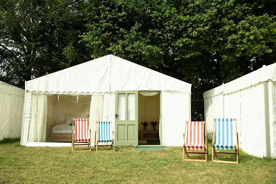 Large luxury safari tent accommodation at Glastonbury Retreat Luxury glamping safari tent with wooden entrance doors and classic striped deckchairs at Glastonbury Retreat