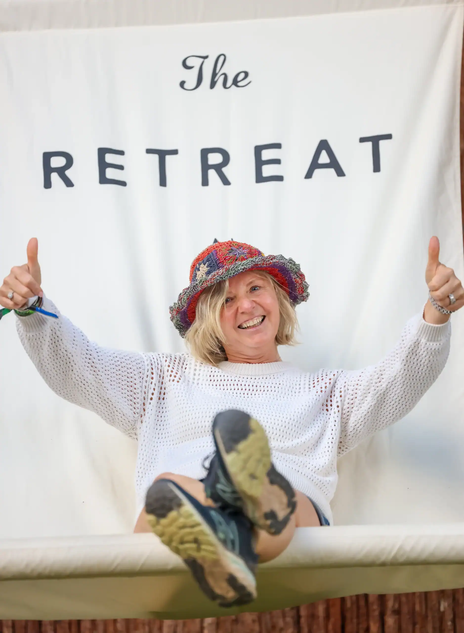 A cheerful festival-goer giving a double thumbs-up whilst enjoying the giant branding deckchair for the off-site Glastonbury Retreat glamping experience.