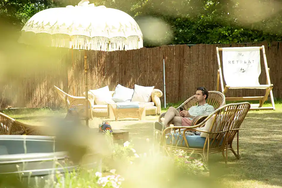 A guest relaxing in comfortable wicker furniture at the outdoor lounge area of The Retreat, showing premium Glastonbury accommodation near Gate B.